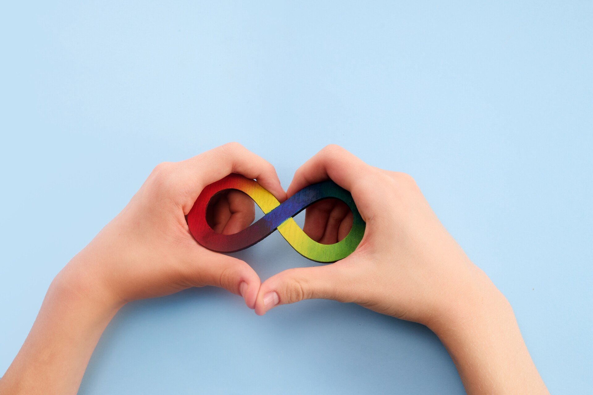 Autism Symbol Hands making a heart shape with a rainbow infinity sign inside the heart.