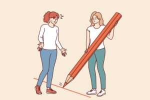 Signs Your Boundaries Are Being Crossed 10 A woman uses a large red pencil to draw a line between her and someone else - setting a boundary.