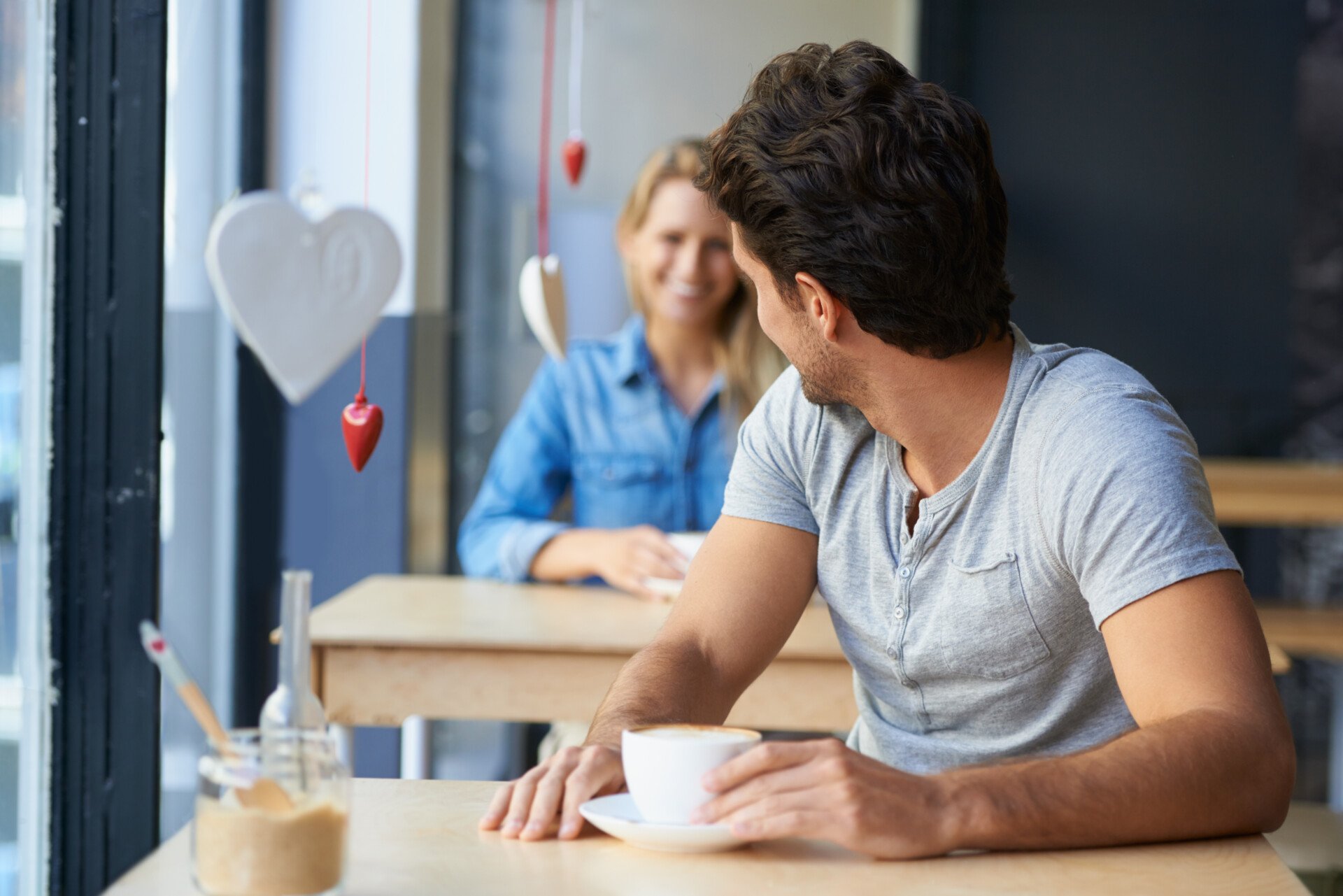 Emotional Cheating A man at a cafe turning around to flirt with a woman sat behind him.