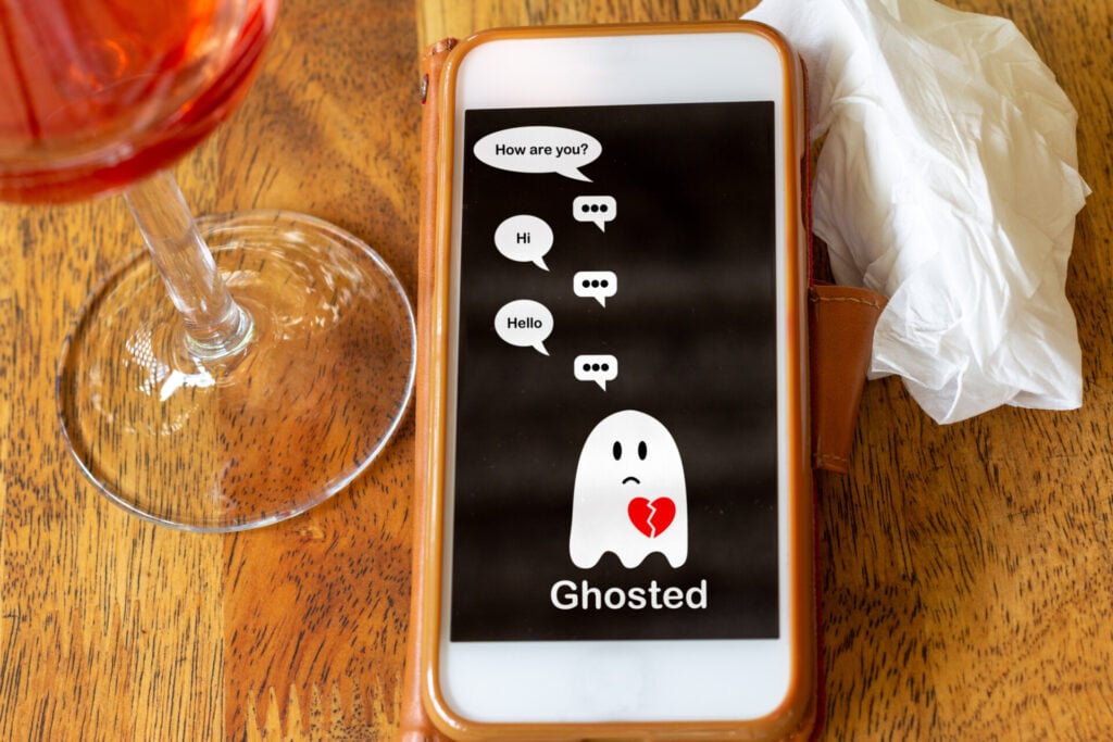 Ghosting In Relationships: Everything You Need To Know 1 Ghosted on mobile phone on table with glass of wine and tissue, Ghosting to cut all communication without explanation, ending a relationship. Social media dating.