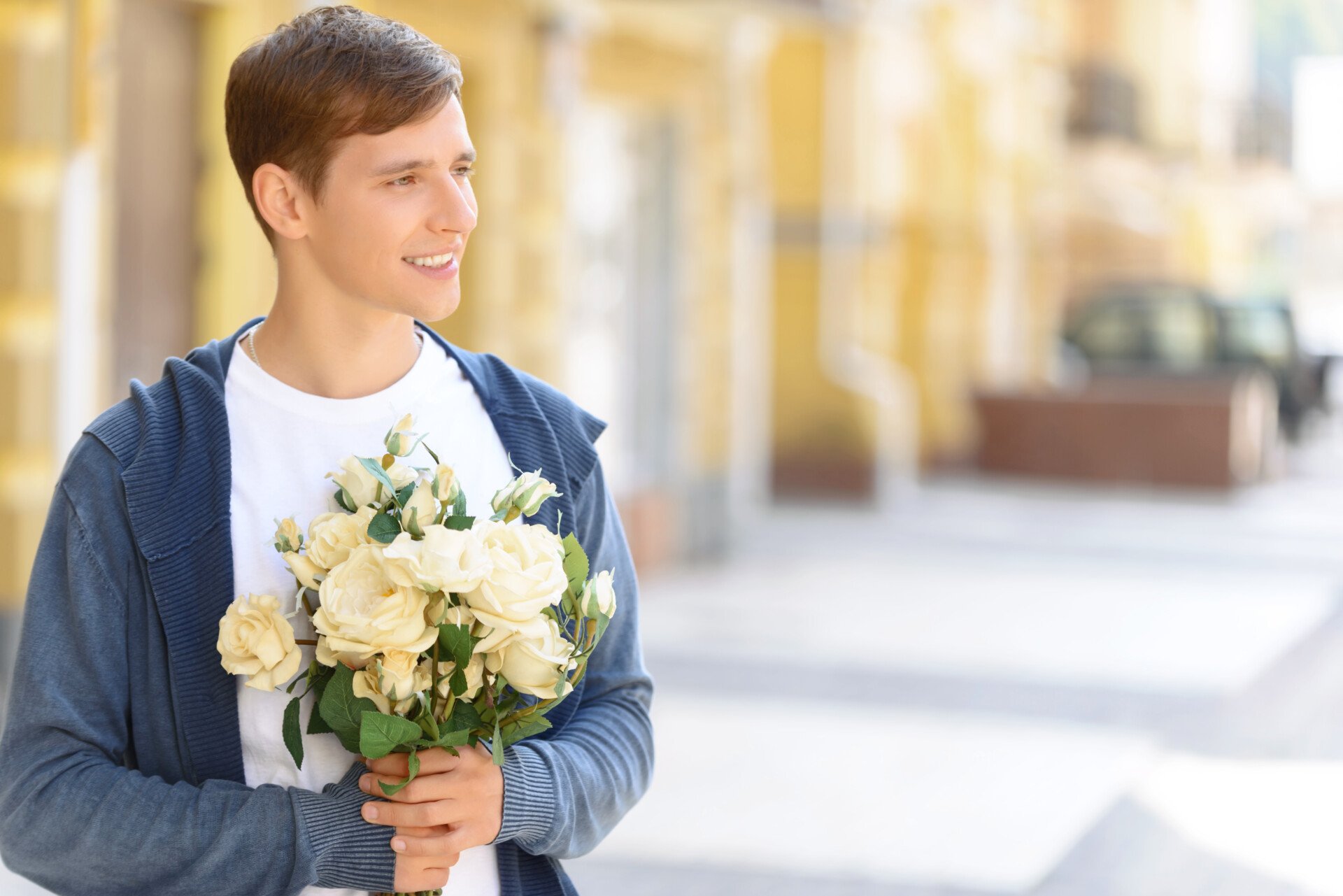 Pleasant cheerful handsome young guy looking aside and holding bouquet of flowers while feeling happy