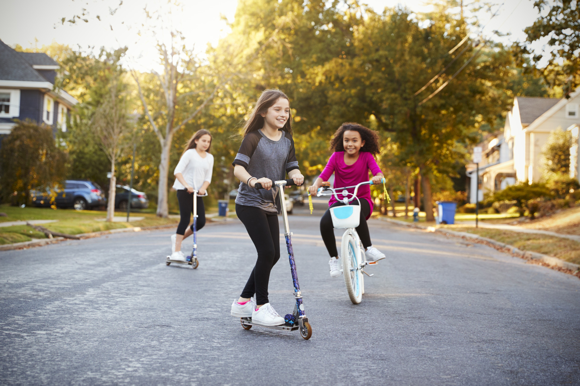 Neighborhood Children 3 children playing on scooters and a bike in their neighborhood.