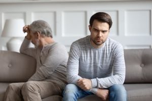 Understanding Passive-Aggressive Parents & How To Cope 3 A father and his adult son sat on a sofa facing away from each other.