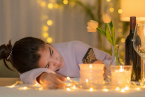 Tired of Being Single 26 A single girl lay with her head on the table looking at her phone. Candles and a bottle of wine on the table.